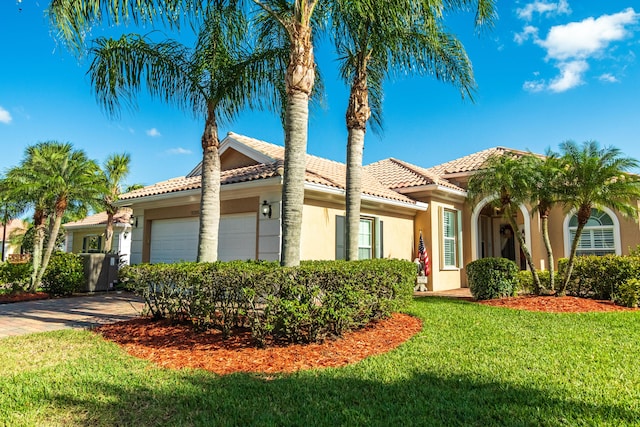 mediterranean / spanish home with an attached garage, driveway, a front lawn, and stucco siding