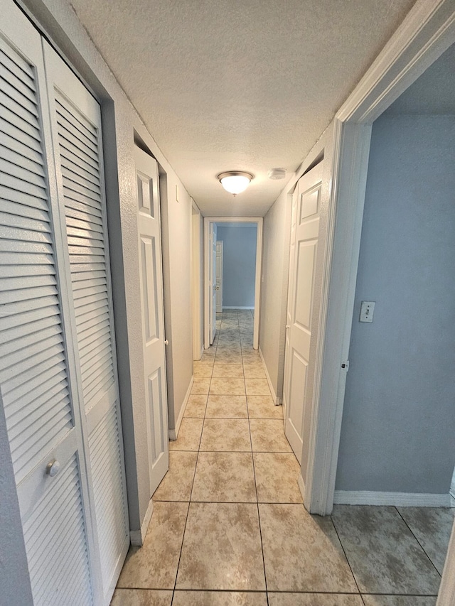 hallway with a textured ceiling, baseboards, and light tile patterned floors