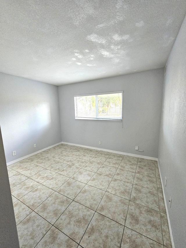 spare room with a textured ceiling, light tile patterned floors, and baseboards