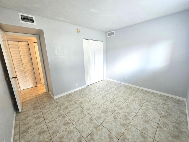 unfurnished bedroom with light tile patterned floors, baseboards, visible vents, and a closet