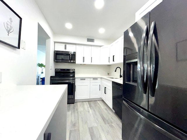 kitchen with white cabinets, light countertops, a sink, and black appliances