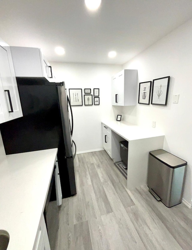 kitchen featuring white cabinetry, light wood-style floors, light countertops, freestanding refrigerator, and built in desk