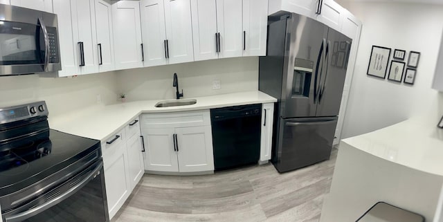 kitchen with white cabinets, black appliances, light countertops, and a sink