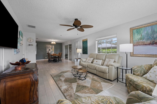 living room with light wood-style flooring, visible vents, ceiling fan, and a textured ceiling