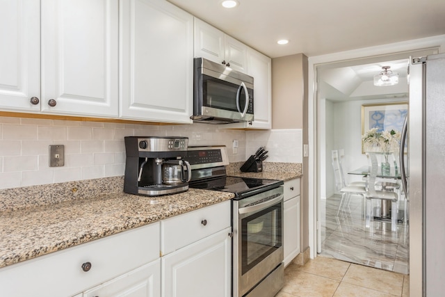 kitchen with light tile patterned floors, stainless steel appliances, white cabinetry, and light stone counters