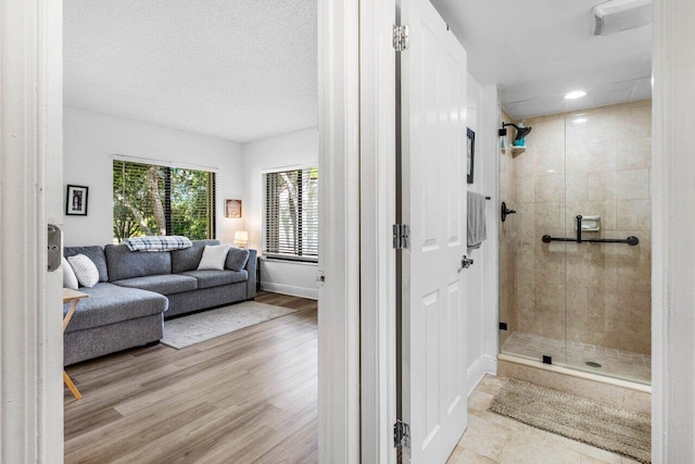 full bathroom featuring a stall shower, a textured ceiling, baseboards, and wood finished floors