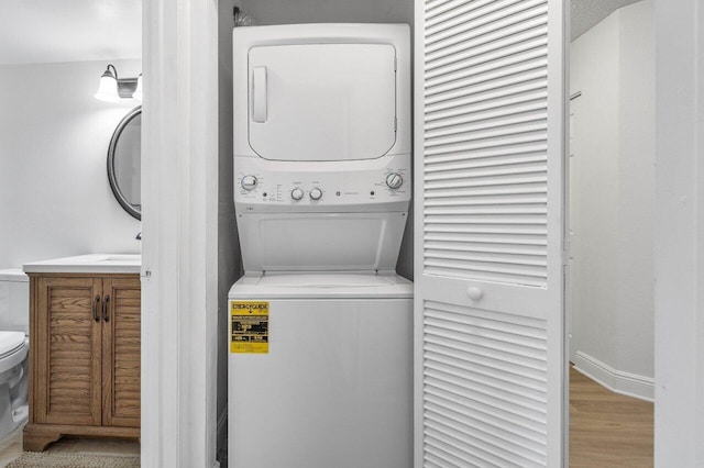 washroom featuring laundry area, stacked washer / dryer, wood finished floors, and baseboards