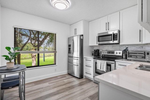 kitchen featuring appliances with stainless steel finishes, white cabinets, a toaster, and tasteful backsplash