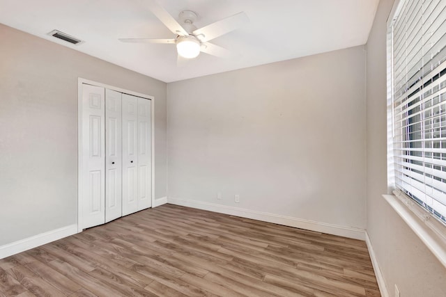 unfurnished bedroom featuring a closet, visible vents, ceiling fan, wood finished floors, and baseboards