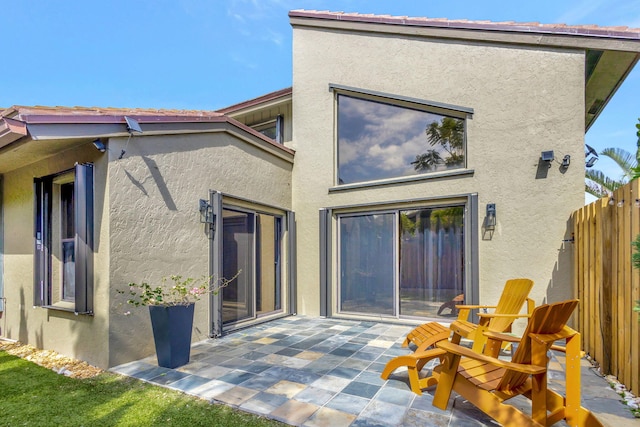 rear view of house with a patio area, fence, and stucco siding