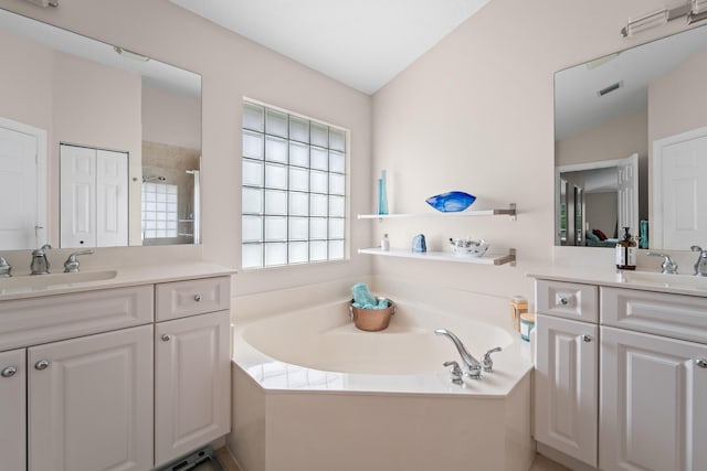 full bath featuring a closet, two vanities, a sink, and a bath