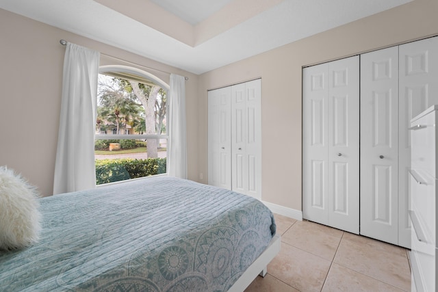 bedroom with light tile patterned floors, baseboards, and multiple closets