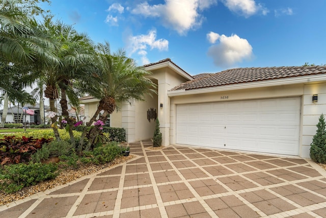 view of front of property with a garage, a tiled roof, decorative driveway, and stucco siding