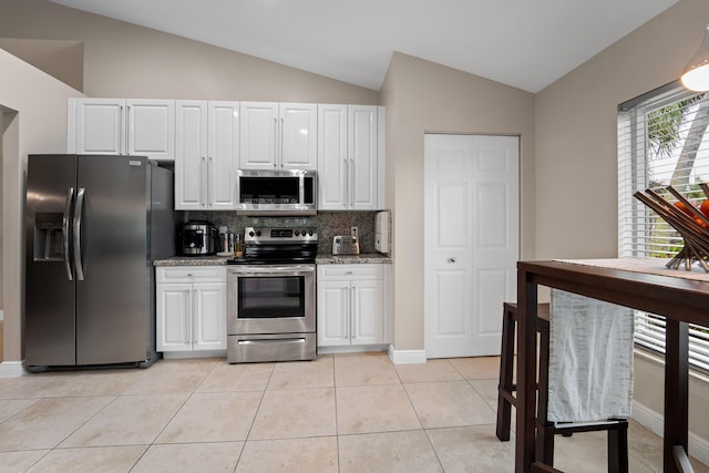 kitchen with light stone counters, light tile patterned floors, lofted ceiling, appliances with stainless steel finishes, and white cabinets