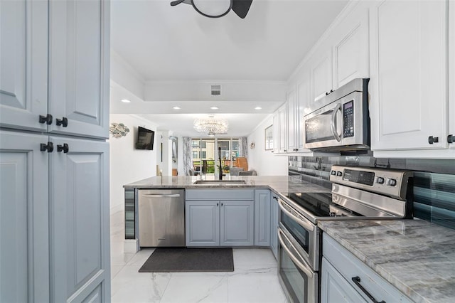 kitchen featuring crown molding, backsplash, appliances with stainless steel finishes, a sink, and a peninsula