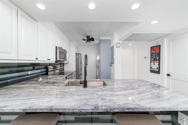 kitchen with a breakfast bar, stainless steel appliances, recessed lighting, white cabinets, and light stone countertops