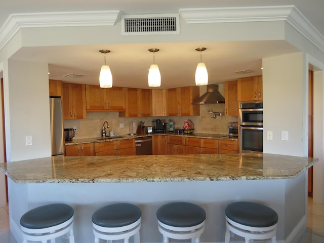 kitchen with wall chimney range hood, a sink, stainless steel appliances, brown cabinets, and tasteful backsplash