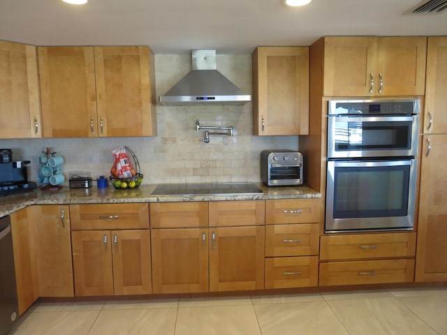 kitchen featuring wall chimney exhaust hood, appliances with stainless steel finishes, dark stone counters, brown cabinetry, and tasteful backsplash