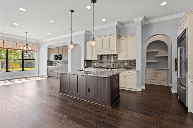 kitchen with tasteful backsplash, arched walkways, cream cabinetry, and dark wood finished floors