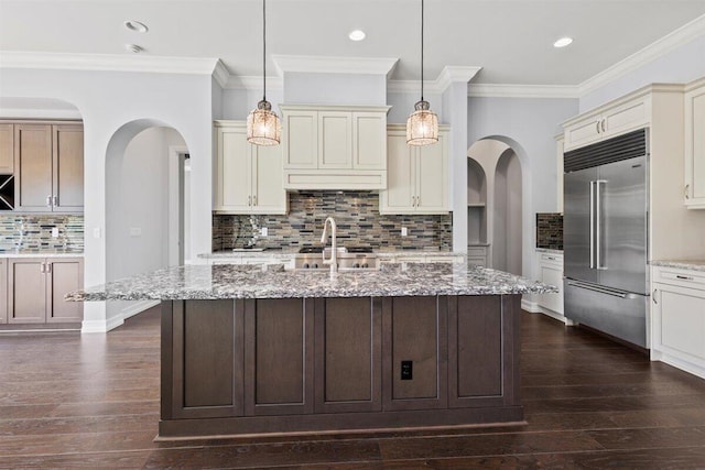 kitchen featuring dark wood-style flooring, cream cabinets, built in refrigerator, and light stone counters