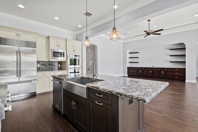 kitchen featuring built in appliances, arched walkways, dark wood-style flooring, a sink, and cream cabinetry