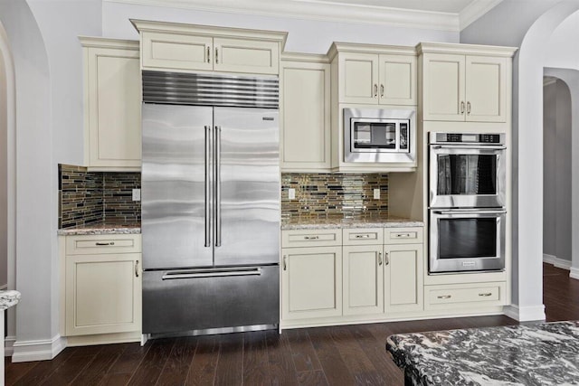 kitchen featuring built in appliances, cream cabinets, and arched walkways