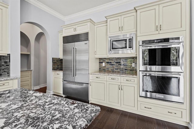 kitchen featuring stone counters, crown molding, cream cabinets, and built in appliances