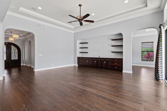 unfurnished living room featuring dark wood-style floors, arched walkways, a raised ceiling, and ornamental molding