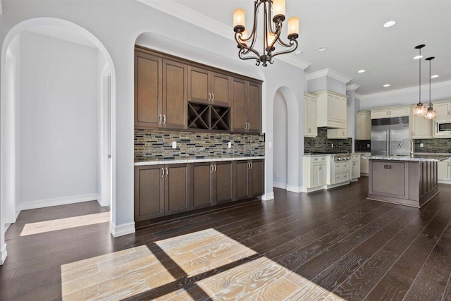 kitchen with arched walkways, dark wood-style floors, ornamental molding, built in refrigerator, and backsplash