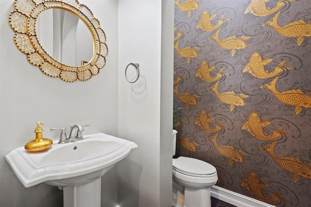 half bathroom featuring toilet, baseboards, and a sink