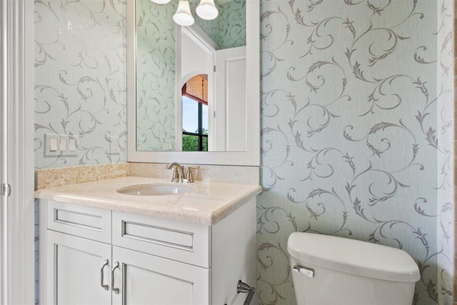 half bathroom with vanity, toilet, and wallpapered walls