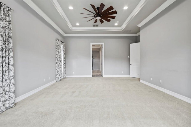 empty room featuring light carpet, baseboards, a raised ceiling, ceiling fan, and ornamental molding