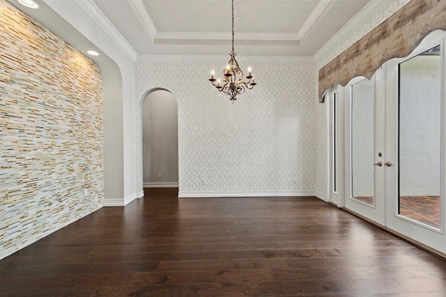 unfurnished dining area featuring wallpapered walls, arched walkways, wood finished floors, a tray ceiling, and crown molding