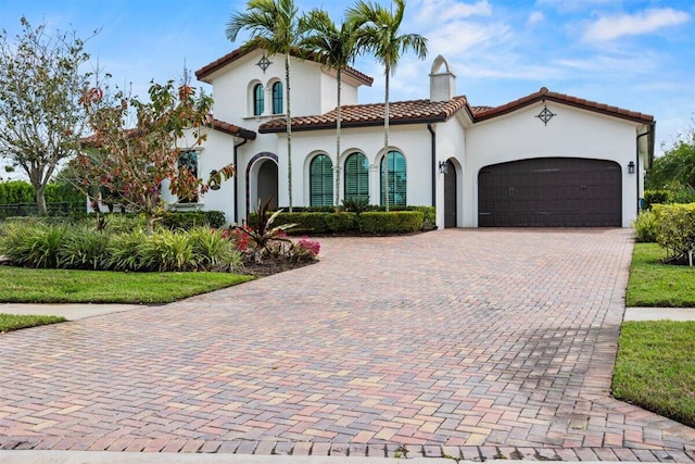 mediterranean / spanish-style home featuring a garage, a tiled roof, decorative driveway, and a chimney