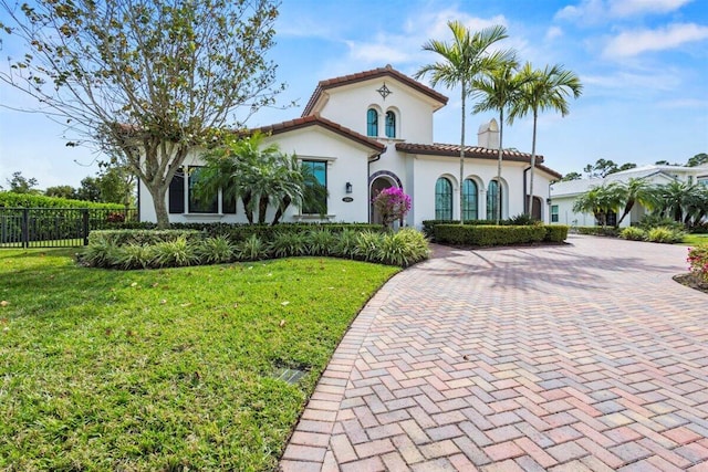 mediterranean / spanish-style home with fence, a tile roof, decorative driveway, stucco siding, and a front yard