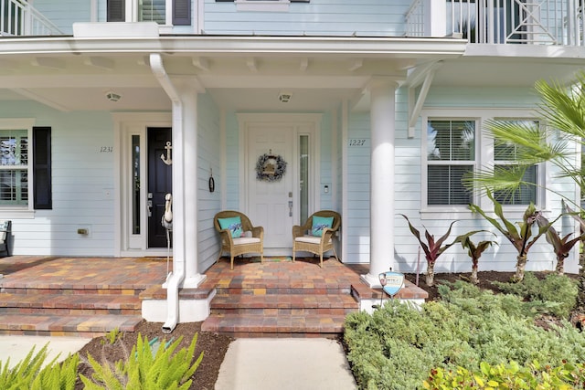 view of exterior entry with covered porch and a balcony