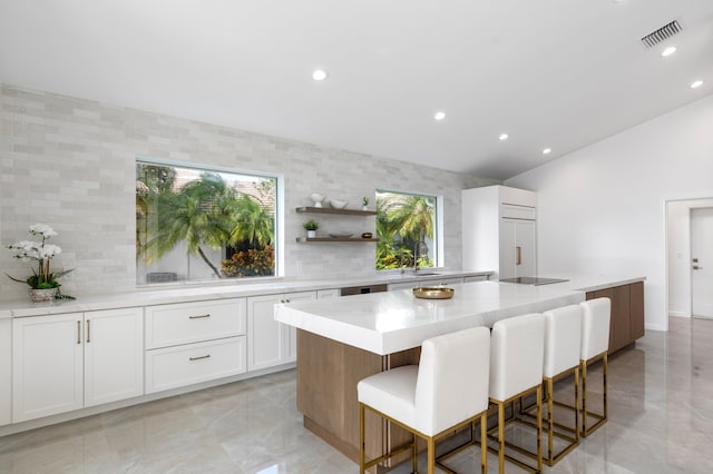 kitchen with a center island, a breakfast bar area, open shelves, visible vents, and white cabinets