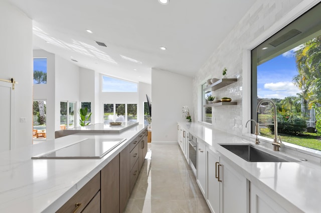 kitchen featuring light stone counters, black electric cooktop, a sink, white cabinetry, and open shelves