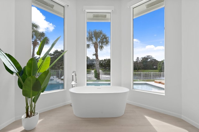 full bath featuring a water view, a freestanding bath, baseboards, and wood finished floors