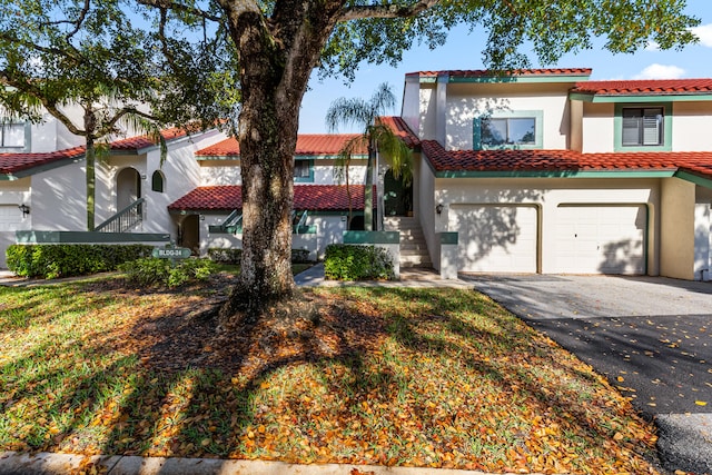 mediterranean / spanish-style house featuring aphalt driveway, a tiled roof, an attached garage, and stucco siding