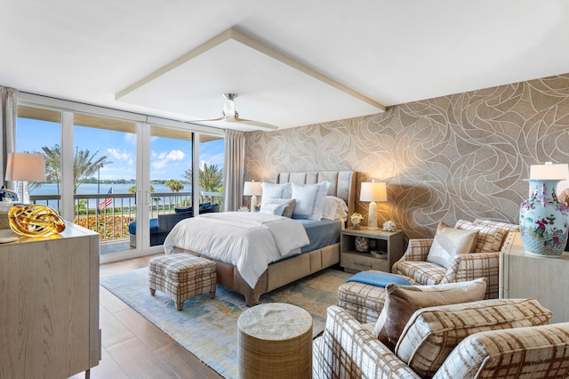 bedroom featuring access to exterior, a wall of windows, a water view, and wallpapered walls