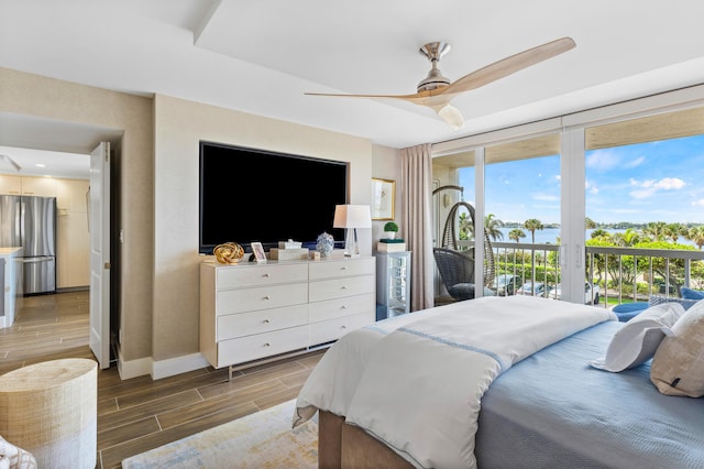 bedroom featuring baseboards, access to exterior, freestanding refrigerator, wood tiled floor, and expansive windows