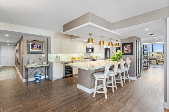 kitchen featuring beverage cooler, stainless steel appliances, wood finish floors, and pendant lighting