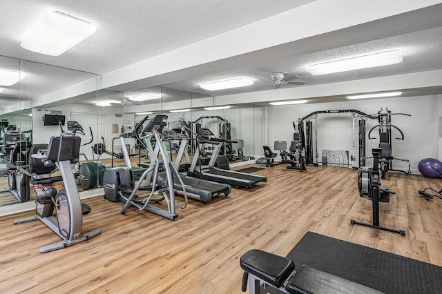 exercise room featuring light wood-type flooring, ceiling fan, and a textured ceiling