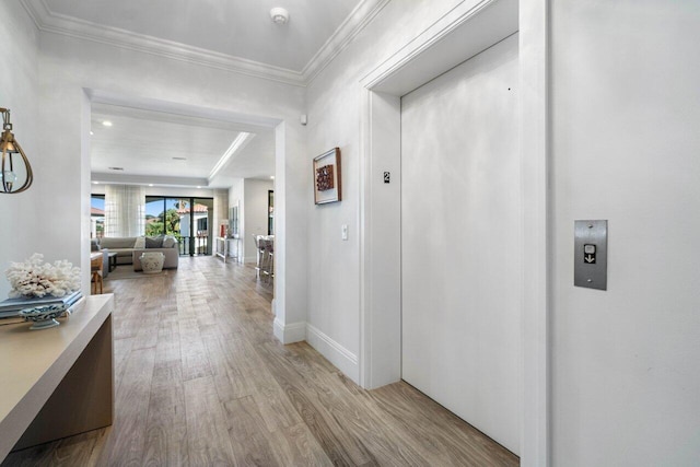 hall with light wood-type flooring, elevator, crown molding, and baseboards