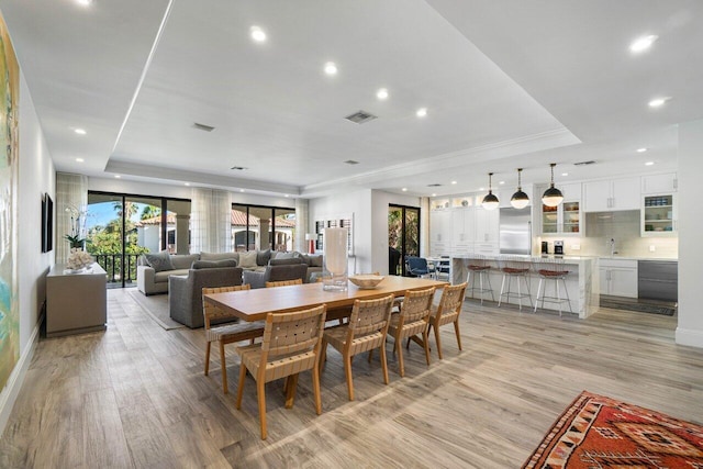 dining area with light hardwood / wood-style floors and a raised ceiling