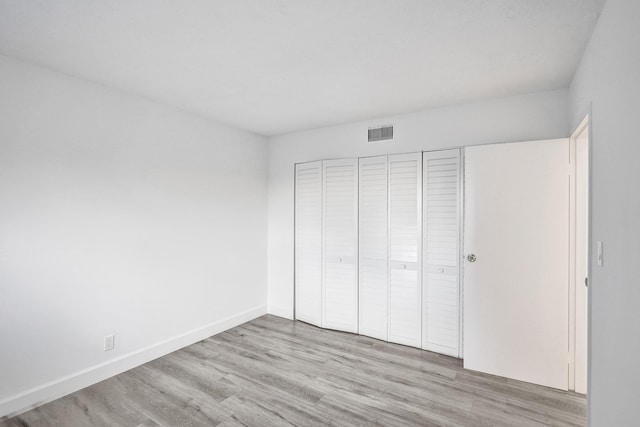 unfurnished bedroom featuring baseboards, a closet, visible vents, and wood finished floors