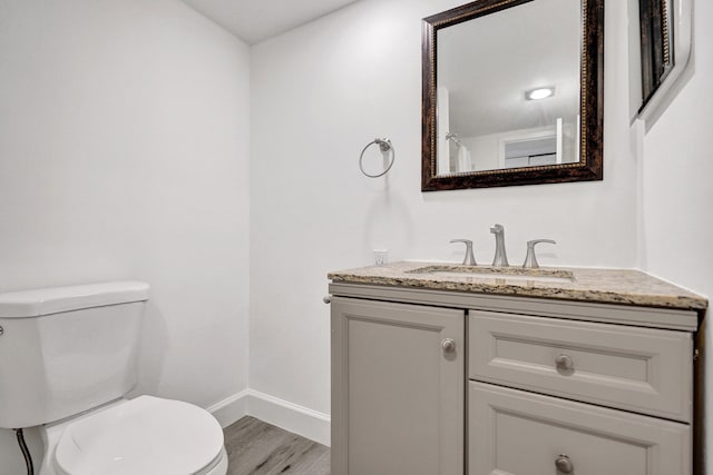 bathroom with toilet, baseboards, wood finished floors, and vanity