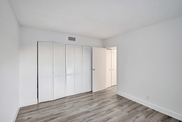 unfurnished bedroom with a closet, visible vents, baseboards, and wood finished floors