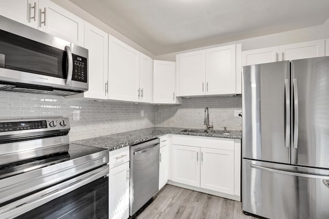 kitchen featuring white cabinets, dark stone counters, appliances with stainless steel finishes, a sink, and backsplash